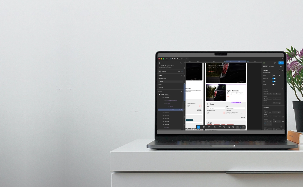 The Delta Design System Figma file open on a laptop on a desk with a book and a flower pot